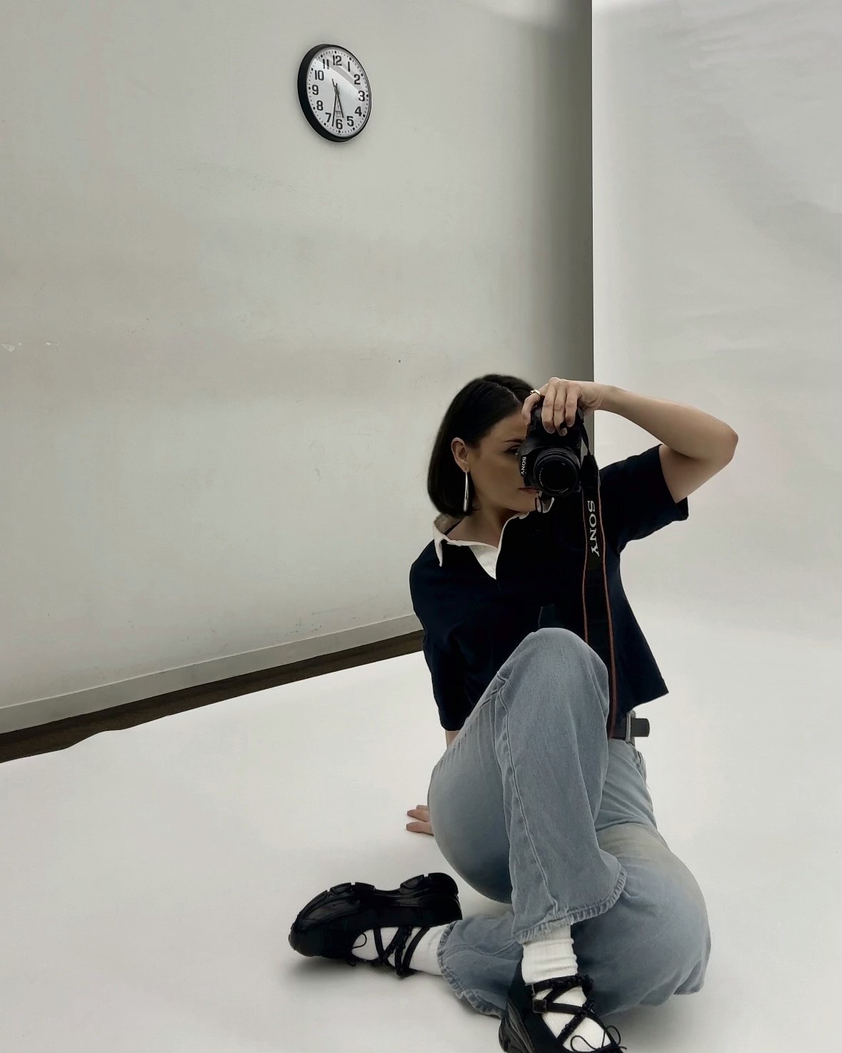 Jordan Mead seated on a white studio floor, holding a camera up to her face